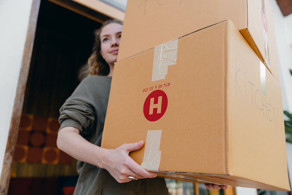 A white moving van is parked on the street outside a white residential building, part of a home relocation process. The van's side door is closed, and it appears ready for furniture transport or packi
