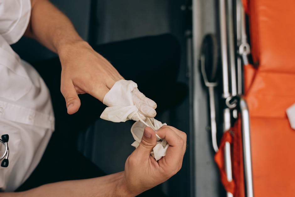 Close-up of a person wearing a white uniform and latex gloves, carefully wrapping a piece of protective tissue around their fingers in preparation for a home relocation. The setting appears to be inside a moving vehicle, with an orange moving blanket or cover partially visible on the right side and various tools and packing materials arranged nearby on a work surface. The person's hands are focused on the packing task, indicating a professional packing process essential for secure furniture transport and loading during a same-day emergency removals service in Harringay offered by Man and Van Harringay. The image highlights the meticulous handling involved in packing fragile items or securing furniture for transport, reflecting the logistics and care required in professional removals and packing services.